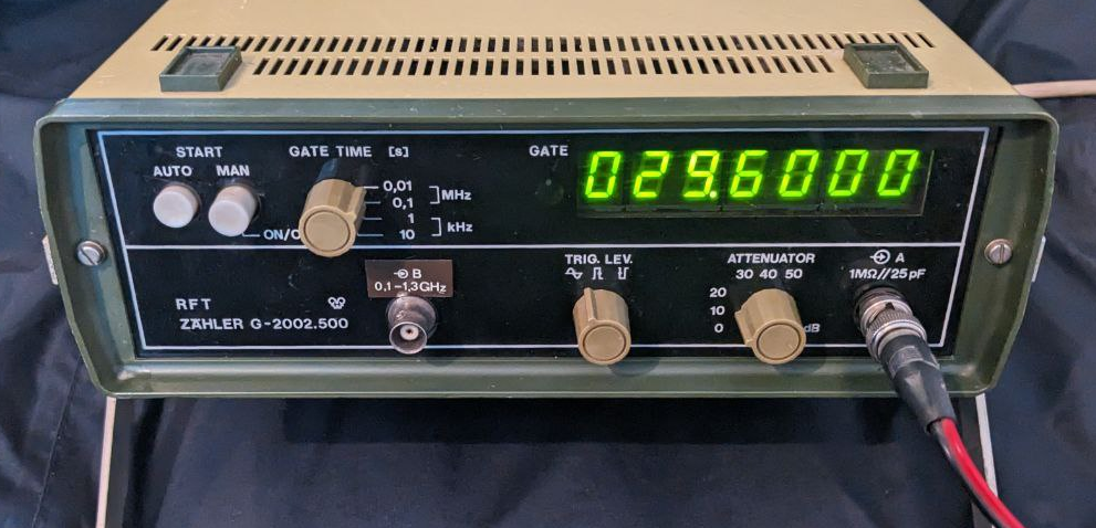 1) Kurzbeschreibung: Frontansicht eines Frequenzzählers mit leuchtend grünem 7‑Segment‑Display und der Anzeige „029.6000“, mehreren Drehknöpfen, Tastern und BNC‑Anschlüssen.	
<ol start=