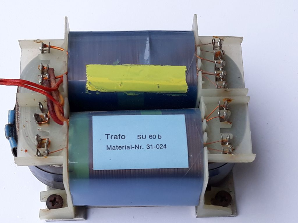 Dieser Alt-Text wurde noch nicht überprüft.
<p>Kurzbeschreibung: Ein Transformator mit zwei Wicklungen und seitlichen Anschlussleisten, von oben auf weißem Hintergrund fotografiert.</p>
<p>Detaillierte Beschreibung: Das Gerät besteht aus einem rechteckigen Blechkern mit zwei nebeneinander liegenden Spulenkörpern, die mit blaugrünem Isoliermaterial umwickelt sind. Auf der oberen Spule klebt mittig ein gelber Streifen, auf der unteren Spule ein hellblaues Etikett mit der Aufschrift „Trafo  SU 60 b“ und „Material-Nr. 31-024“. An beiden Stirnseiten befinden sich helle Kunststoffträger mit Reihen von metallischen Lötfahnen; daran sind feine, lackierte Kupferdrähte angeschlossen, teils mit sichtbaren Lötstellen und leichten Anlaufspuren. Links führen zwei rote flexible Leitungen zu einer Anschlussseite; daneben ist ein kleines blaues zylindrisches Element zu sehen. Unten sind Montagewinkel mit Schrauben erkennbar. Der Hintergrund ist einheitlich weiß, das Foto zeigt das Bauteil leicht von oben.">
<figcaption>Abbildung E-5.3.2: Trafo mit sichtbar getrennten Wicklungen</figcaption></p>
</figure>
</aside>
Ein Transformator dient zur Umsetzung einer hohen Wechselspannung z. B. $230&nbsp;V$ in eine 
niedrigere Wechselspannung z. B. $13,8&nbsp;V$. Ein Transformator kann nur Wechselspannungen übertragen. Legt man unerlaubt eine Gleichspannung an einen Transformator an, wirkt dieser aufgrund des geringen ohmschen Widerstands der Primärwicklung wie ein Kurzschluss. Der Transformator kann dadurch stark überhitzen und im schlimmsten Fall durchbrennen.
<hr />
<p>Das Übersetzungsverhältnis eines Transformators lässt sich wie folgt angeben:</p>
<p>$ü = \frac{N_P}{N_S} = \frac{U_P}{U_S}$</p>
<p>Das Verhältnis der Windungszahlen entspricht somit dem Verhältnis der Spannungen. Durch Umstellen dieser Grundgleichung lassen sich sowohl die Spannungen $U$ als auch die Windungszahlen $N$ auf der Primär- oder Sekundärseite berechnen.</p>
<aside class=