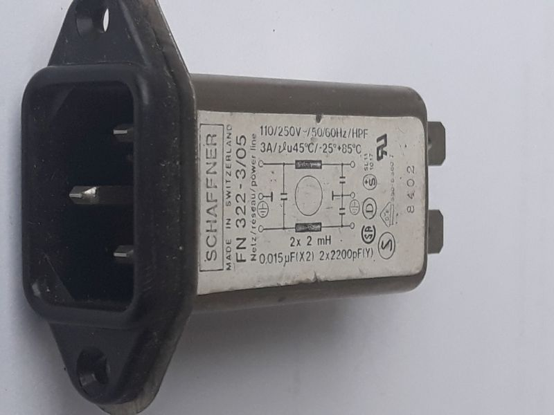 Dieser Alt-Text wurde noch nicht überprüft.
<ol>
<li>
<p>Kurzzusammenfassung: Ein flanschmontierbarer IEC-Netzeinbaustecker mit integriertem Filter von Schaffner liegt auf weißem Hintergrund.</p>
</li>
<li>
<p>Detaillierte Beschreibung: Links ist die schwarze Kunststofffront mit einem dreipoligen IEC-C14-Einlass und zwei Befestigungsbohrungen zu sehen, daran schließt sich ein längliches Metallgehäuse an. Auf der Oberseite klebt ein weißes Typenschild mit der Aufschrift „SCHAFFNER – MADE IN SWITZERLAND – FN 322-…“, mit Angaben wie „110/250 V~ 50/60 Hz“ und „3 A“, einem kleinen Schaltbild (mit Beschriftungen „2× 2 mH“, „0,015 µF (X2)“ und „2× 2200 pF (Y)“) sowie mehreren Prüf- und Zulassungszeichen. Rechts ragen zwei Flachsteckkontakte aus dem Gehäuse heraus; an der Seite ist eine Zahl (z. B. „8402“) aufgedruckt. Die Aufnahme ist leicht seitlich gedreht, die Farben sind Schwarz, Grau und Weiß, mit leichten Gebrauchsspuren am Gehäuse."></p>
 <figcaption>Abbildung A-5.9.6:  Filter direkt am $230&nbsp;V$ AC Spannungseingang</figcaption>
</li>
</ol>
</figure>
</aside>

                        </div>
                    </article>
                </main>

                <aside class=