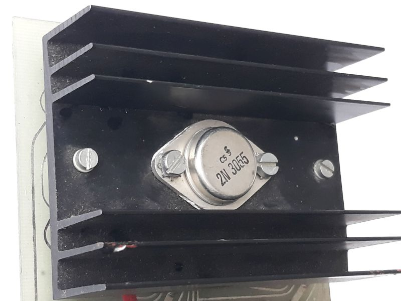 Dieser Alt-Text wurde noch nicht überprüft.
<ol>
<li>
<p>Kurze Zusammenfassung: Nahaufnahme eines schwarzen Kühlkörpers mit mehreren Lamellen und einem zentral montierten Metallbauteil mit der Aufschrift „2N3055“.</p>
</li>
<li>
<p>Detaillierte Beschreibung: Im Bild dominiert ein schwarzer Aluminium-Kühlkörper mit vier horizontalen Kühlrippen, montiert auf einer schwarzen Trägerplatte. In der Mitte sitzt ein silbernes, rundes Metallgehäuse mit ovaler Grundplatte, das mit zwei Schrauben befestigt ist; darauf sind „C5“ und „2N3055“ lesbar. Links und rechts in der Trägerplatte befinden sich zusätzlich zwei weitere Schlitzschrauben. Am Rand des Metallgehäuses sind helle, unregelmäßige Rückstände sichtbar. Unten ragt der Rand einer Leiterplatte mit feinen Leiterbahnen ins Bild; am unteren linken Bereich ist ein kurzes Stück einer rot isolierten Leitung zu sehen. Der Hintergrund ist weiß, die Beleuchtung erzeugt leichte Reflexe auf Metall und Lackflächen."></p>
 <figcaption>Abbildung NEA-10.15.4: Der Längstransistor in einem linear geregelten Netzteil muss große Verlustleistungen aushalten und wird deshalb auf einen Kühlkörper montiert.</figcaption>
</li>
</ol>
</figure>
</aside>
<section class=