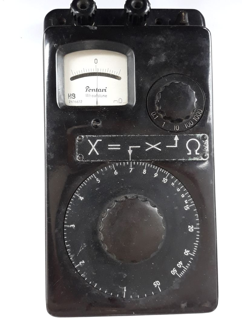 Dieser Alt-Text wurde noch nicht überprüft.
<ol>
<li>
<p>Kurze Zusammenfassung: Schwarzes Messgerät mit analogem Zeigerinstrument, großem Drehring, zusätzlichem Drehschalter und mehreren Anschlussklemmen.</p>
</li>
<li>
<p>Detaillierte Beschreibung: Das Gerät hat ein rechteckiges, schwarzes Gehäuse und liegt auf weißem Untergrund. Oben links befindet sich ein rechteckiges Analoginstrument mit gebogener Skala und der mittigen Markierung „0“; auf der Skalenfläche steht „Pontavi Wheatstone“ sowie ein Ω-Symbol. Oben am Rand sitzen zwei schwarze Schraubklemmen; rechts oben sind zwei kleine, stiftartige Anschlüsse zu sehen. Rechts neben dem Messwerk ist ein kleinerer Drehschalter mit Skalenring, beschriftet mit 0,1 – 1 – 10 – 100 – 1000. Unterhalb des Messwerks ist eine schmale Metallplakette mit der Aufschrift „X =“ und Symbolen sowie einem Ω-Zeichen verschraubt. Den unteren Bereich dominiert ein großer, runder Drehring mit feiner Teilung und Zahlen von 0 bis 50 (in 5er-Schritten markiert), in dessen Mitte ein griffig ausgeformter Drehknauf sitzt. Das Gehäuse zeigt leichte Kratzer und Gebrauchsspuren; mehrere Schrauben sind sichtbar."></p>
 <figcaption>Abbildung A-4.3.2: Widerstandsmessbrücke nach Wheatstone (Pontavi)</figcaption>
</li>
</ol>
</figure>
<p>Die Abbildung <a class=