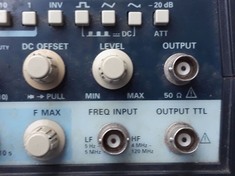 Dieser Alt-Text wurde noch nicht überprüft.
<p>Zusammenfassung: Ausschnitt der Frontplatte eines elektronischen Messgeräts mit mehreren Drehknöpfen und BNC-Buchsen für Ausgang und Frequenzeingang.</p>
<p>Detaillierte Beschreibung: Oben verläuft eine Reihe hellgrauer, quadratischer Tasten mit Symbolen (u. a. Wellenformen) und Beschriftungen wie INV, DC und -20 dB (ATT). Darunter links ein großer, beigefarbener Drehknopf mit der Beschriftung DC OFFSET und dem Hinweis → PULL; in der Mitte ein gleich großer Knopf LEVEL mit Skala von MIN bis MAX. Rechts daneben eine silberne, runde BNC-Buchse mit der Beschriftung OUTPUT und 50 Ω sowie einem Warnsymbol. Im unteren, hellblauen Bereich befindet sich links ein weiterer Drehknopf F MAX. In der Mitte ist eine BNC-Buchse unter der Überschrift FREQ INPUT, umgeben von den Angaben LF 5 Hz–5 MHz und HF 4 MHz–120 MHz. Rechts unten eine weitere BNC-Buchse mit der Beschriftung OUTPUT TTL und einem Warnsymbol. Die Front ist dunkelblau mit hellblauen Feldern; die Bedienelemente wirken leicht benutzt.">
<figcaption>Abbildung EA-7.2.5: Sinusgenerator mit 50 Ohm Innenwiderstand</figcaption></p>
</figure>
</aside>
<aside class=