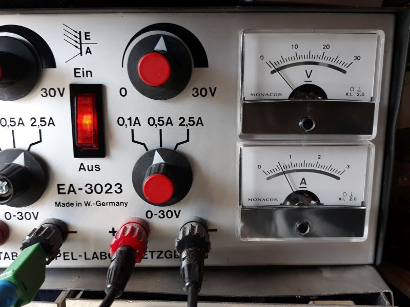 Dieser Alt-Text wurde noch nicht überprüft.
<ol>
<li>
<p>Zusammenfassung: Nahaufnahme der Frontplatte eines Geräts EA‑3023 mit zwei analogen Anzeigen (Volt und Ampere), zwei großen Drehknöpfen, einem rot leuchtenden Wippschalter und mehreren farbigen Anschlussbuchsen mit eingesteckten Leitungen.</p>
</li>
<li>
<p>Detaillierte Beschreibung: Links sind zwei schwarze Drehknöpfe mit roten Mitten zu sehen; um den oberen Knopf ist „0 … 30V“ markiert, um den unteren „0,1A 0,5A 2,5A“. Dazwischen befindet sich ein rechteckiger, rot beleuchteter Wippschalter mit der Beschriftung „Ein“ oben und „Aus“ unten. Darüber steht ein stilisiertes „EA“-Logo, daneben mehrfach „30V“. Im unteren linken Bereich steht „EA‑3023“ und „Made in W.-Germany“. Entlang der unteren Kante sind mehrere 4‑mm‑Buchsen und Stecker sichtbar: u. a. ein grüner, ein roter und ein schwarzer Stecker mit angeschlossenen Kabeln; neben den Buchsen ist „0‑30V“ aufgedruckt. Rechts sind zwei übereinander angeordnete analoge Messwerke der Marke „MONACOR“: oben mit der Skala „0–30“ und dem Symbol „V“ (Volt), unten mit der Skala „0–3“ und dem Symbol „A“ (Ampere); beide Instrumente tragen die Kennzeichnung „Kl. 2.0“. Das Gehäuse wirkt metallisch/silbern, die Beschriftungen sind schwarz, Bedienelemente überwiegend schwarz mit roten Akzenten."></p>
 <figcaption>Abbildung EA-7.2.2: Labornetzgerät mit eingestellter Strombegrenzung auf $500&nbsp;mA$</figcaption>
</li>
</ol>
</figure>
<p>In Labornetzgeräten ist eine Strombegrenzung eingebaut, d.h. übersteigt der Laststrom eine maximale Stromstärke, wird die Klemmenspannung so abgesenkt, dass der Laststrom konstant bleibt. Dies entspricht der Funktion einer Konstantstromquelle -- Bei Kurzschluss an den Ausgangsklemmen fließt der eingestellte maximale Strom.</p>
</aside>
Eine ideale Konstantstromquelle liefert unabhängig von der angeschlossenen Last einen konstanten Dauerstrom. In der Theorie ist dies bei einem unendlichen Innenwiderstand möglich. In der Praxis haben Stromquellen einen sehr hohen Innenwiderstand.
<aside class=